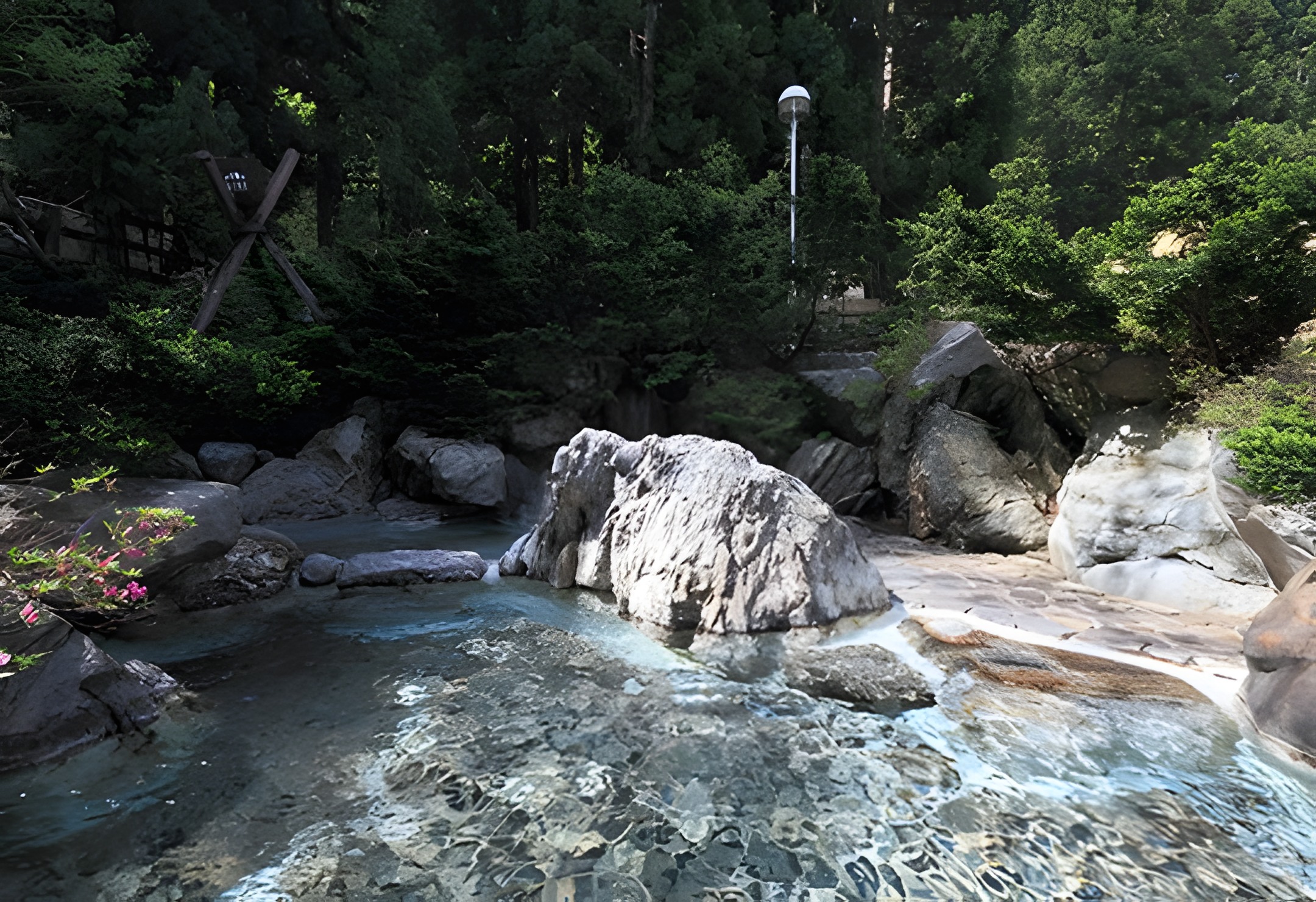 A clear turquoise open-air hot spring pool set among rocks and cedar forest at Ichirino Onsen.